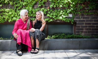 一名身穿亮粉色纱丽的老年妇女与一名被绿叶包围的年轻妇女坐在砖墙上谈笑风生