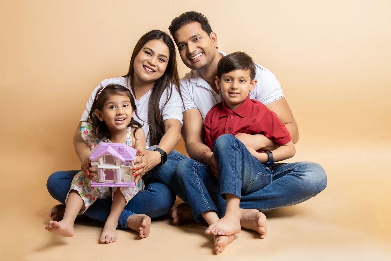 Happy young indian parents and kids wearing casual cloths sitting together on floor isolated over beige studio background. Asian Family bonding.