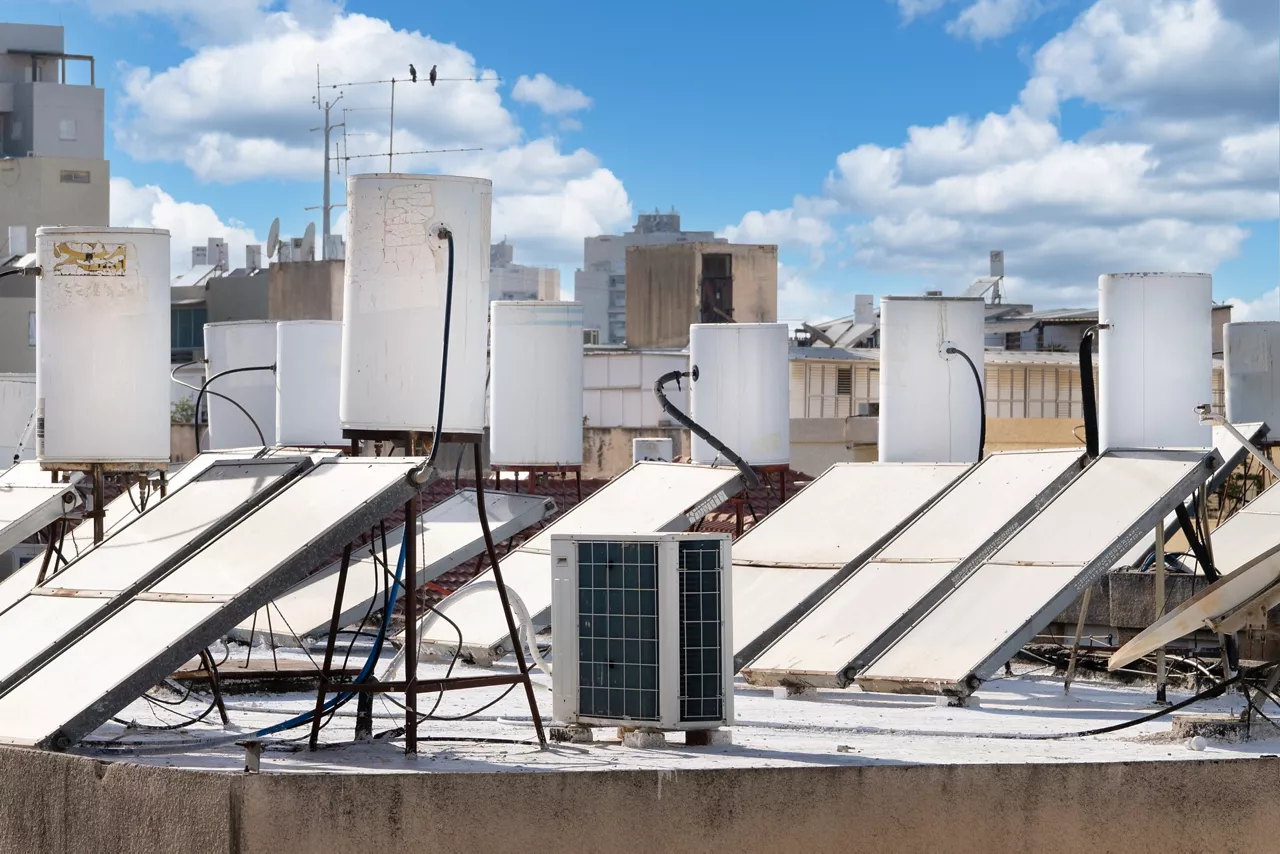 Many solar water heating systems installed on the roof of a residential house on the blue sky with clouds background in Israel. Renewable eco-friendly energy
