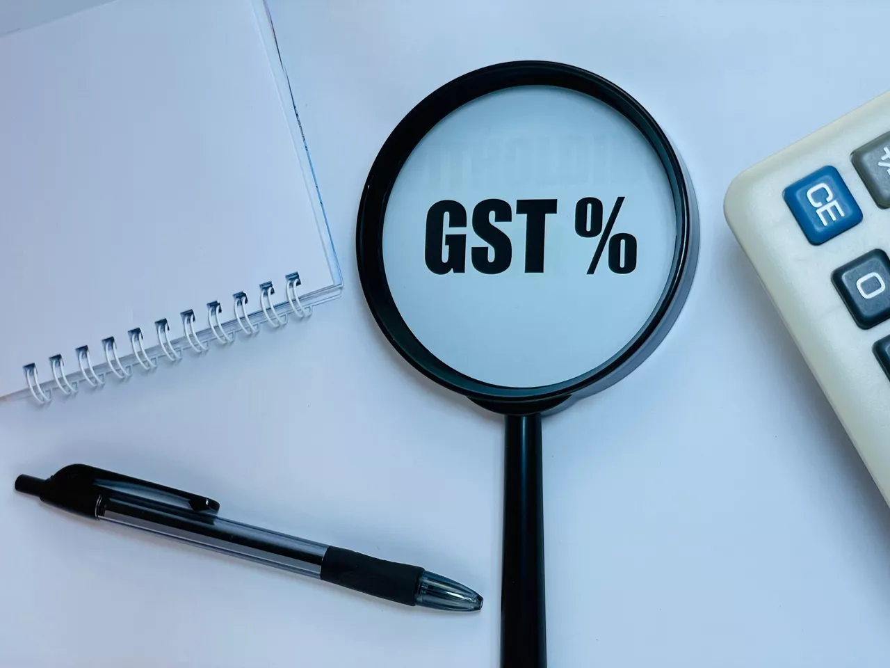 GST (Goods and Services Tax) - acronym on magnifying glass on a white background with calculator, notebook and pen. Business and finance concept