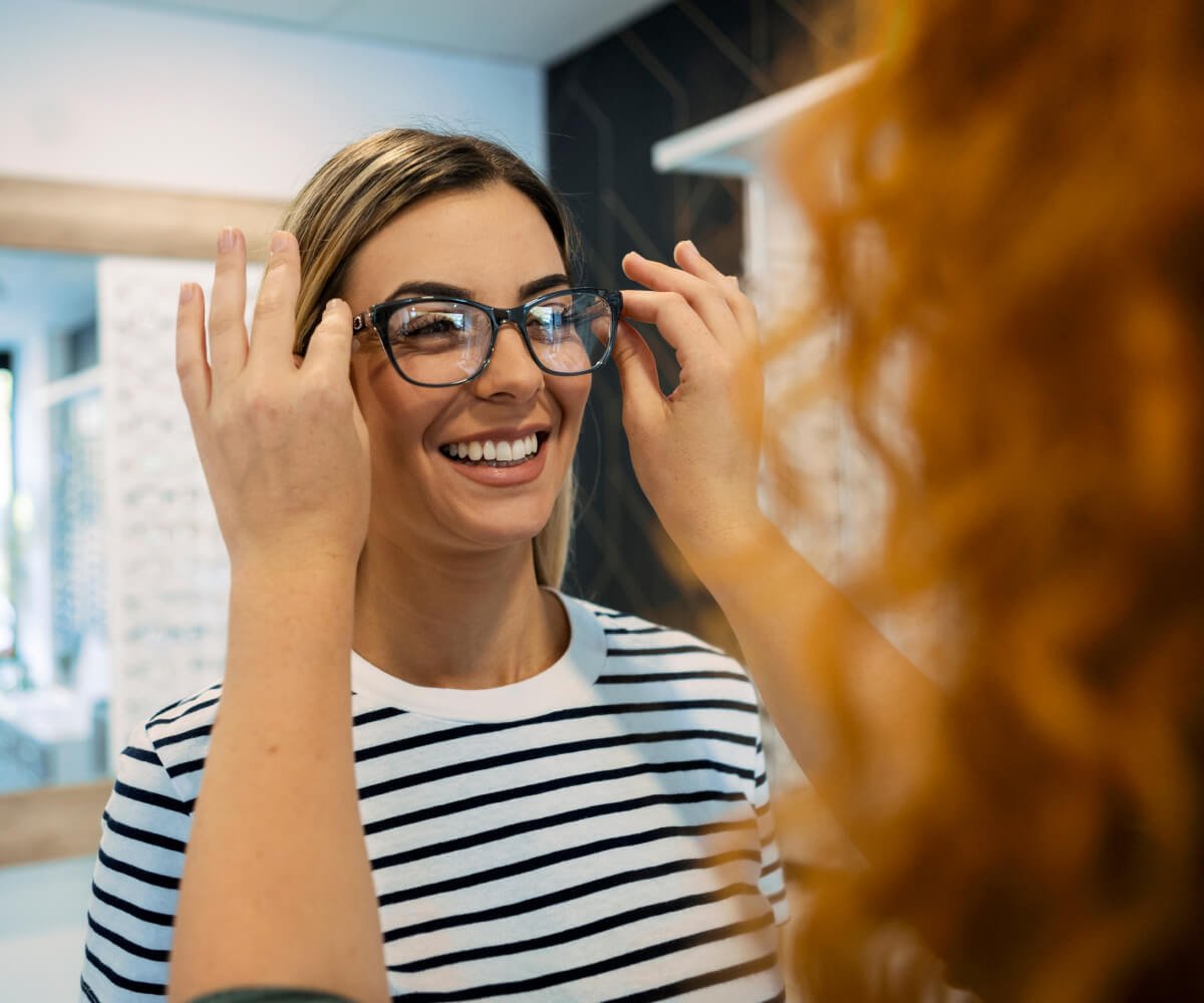 A woman smiles joyfully while examining a pair of glasses in her hands