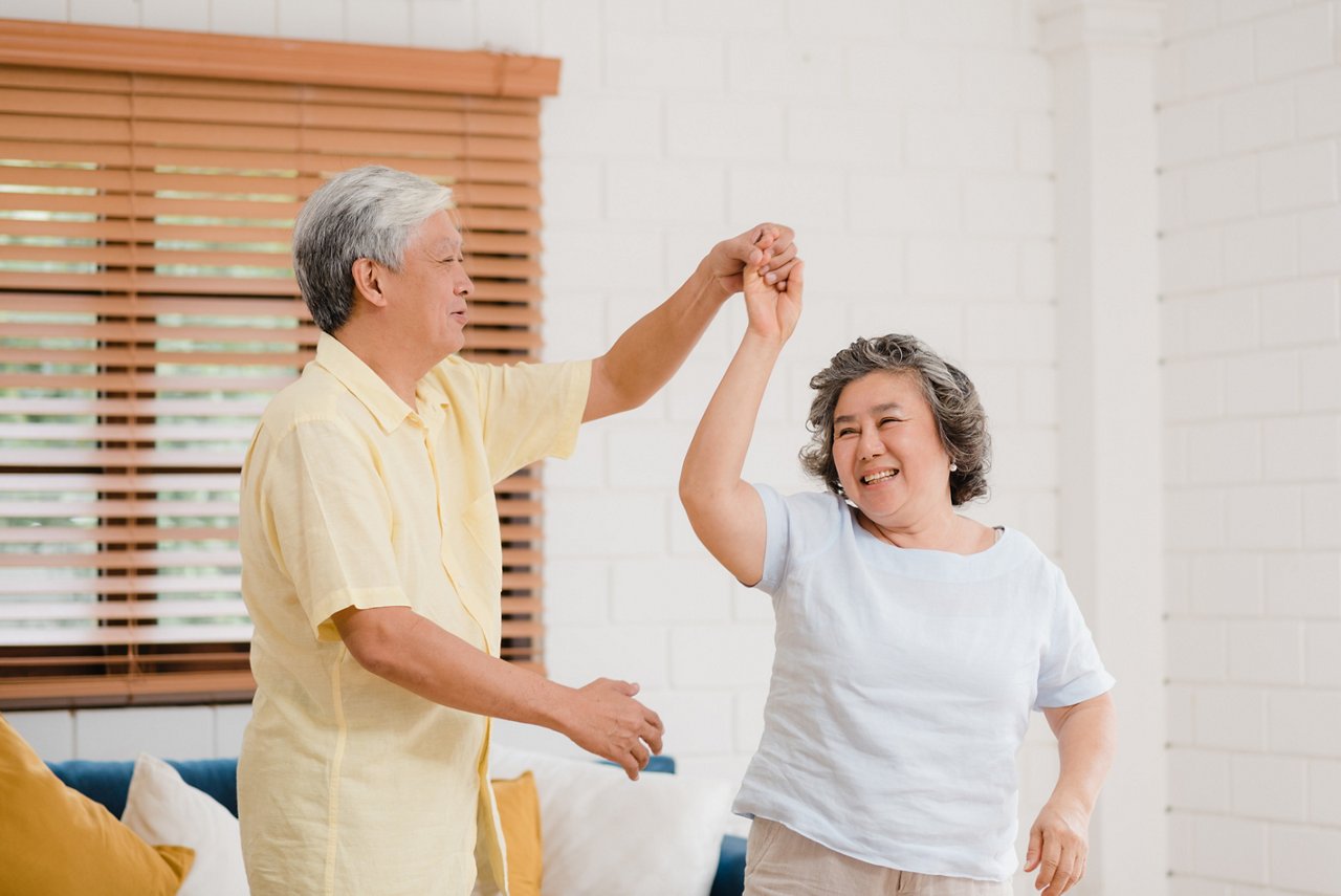 Asian elderly couple dancing together while listen to music in living room at home, sweet couple enjoy love moment while having fun when relaxed at home. Lifestyle senior family relax at home concept.
