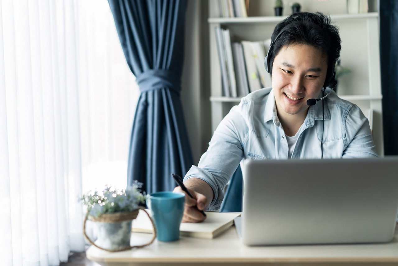 An Asian man attending an online meeting in his home office
