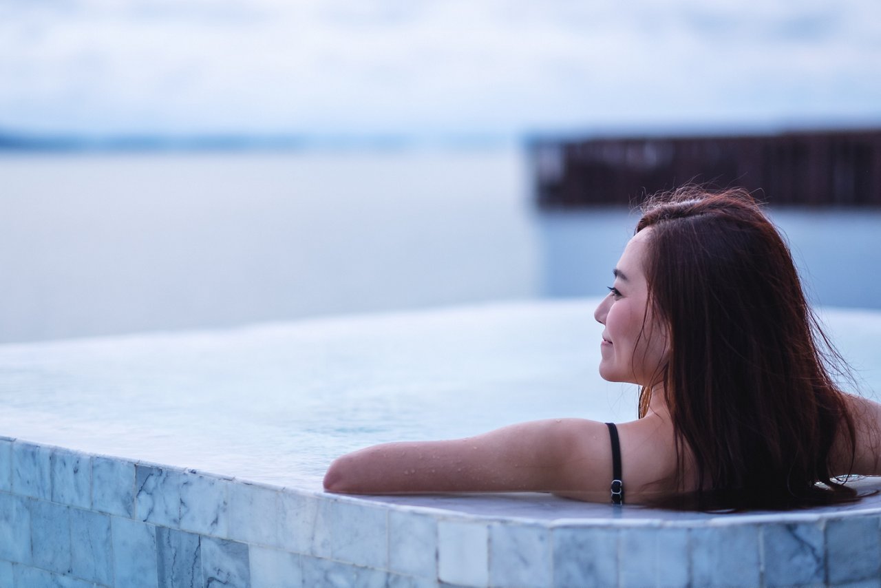 Young Asian woman in a pool by the beach with a faraway look 