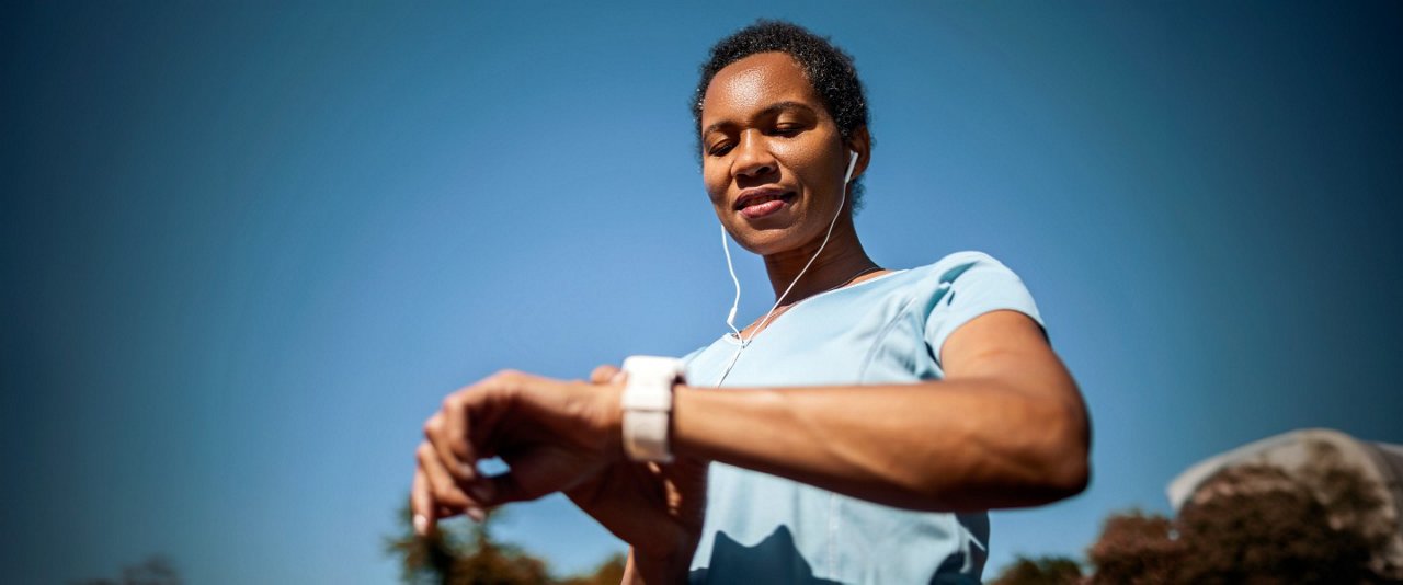 A woman wearing headphones, checking the time on her wristwatch.