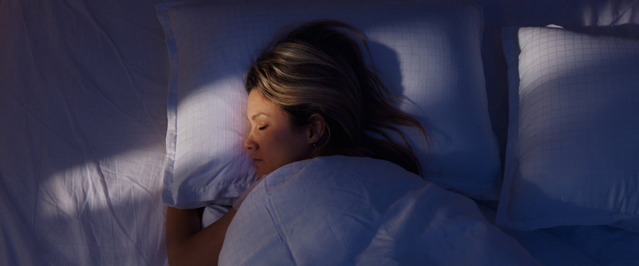 A woman peacefully sleeping in bed, surrounded by soft pillows, enjoying a restful night's sleep.