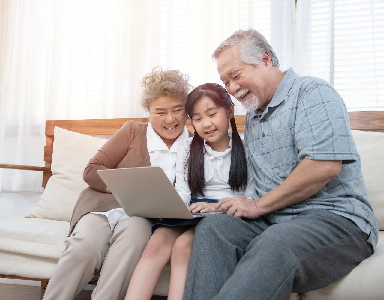 Little granddaughter teach senior elder to surf internet using computer and technology& modern lifestyle.Happy asian grandparent with little young cute grandchild sitting on sofa playing laptop together..
