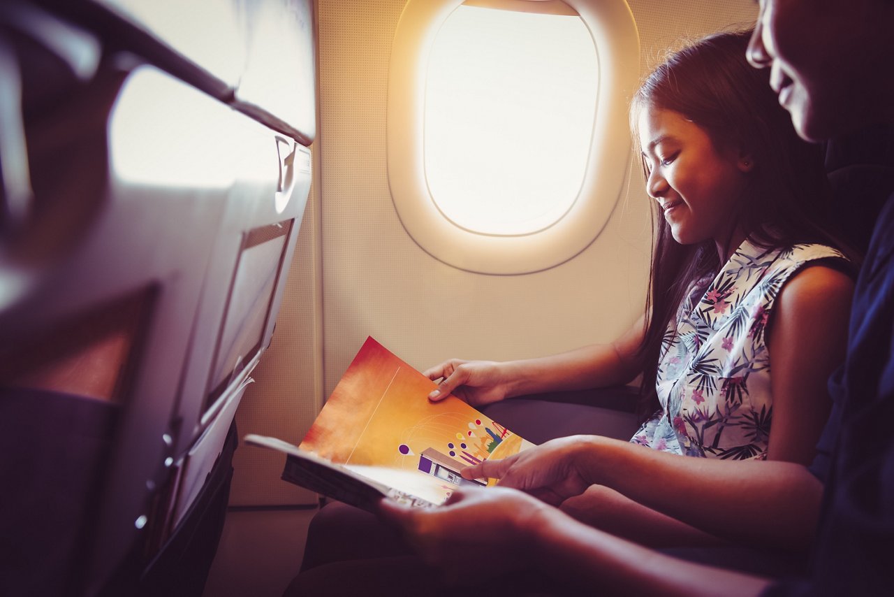Young girl sitting on a window seat and reading on the plane