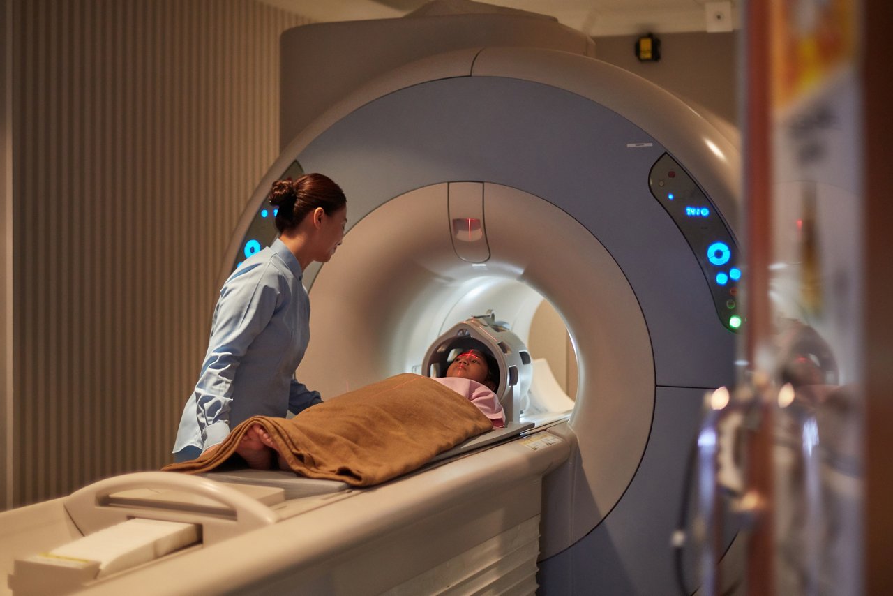 A girl is undergoing a tomography examination, monitored by a female nurse