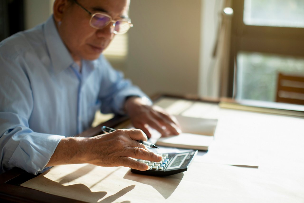 Man writes on a piece of paper with an open laptop on a table.