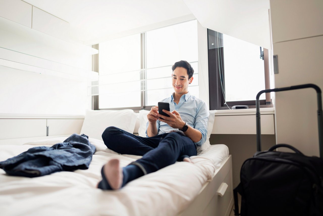 Young Asian man using his mobile phone in a hotel room.