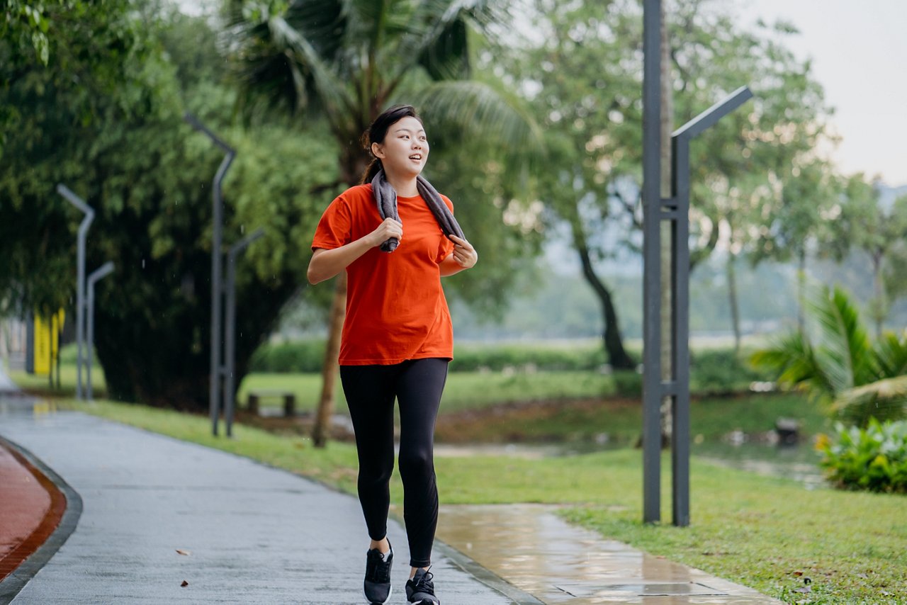 An Asian woman wearing bright sports clothing runs in the street on a sunny day.