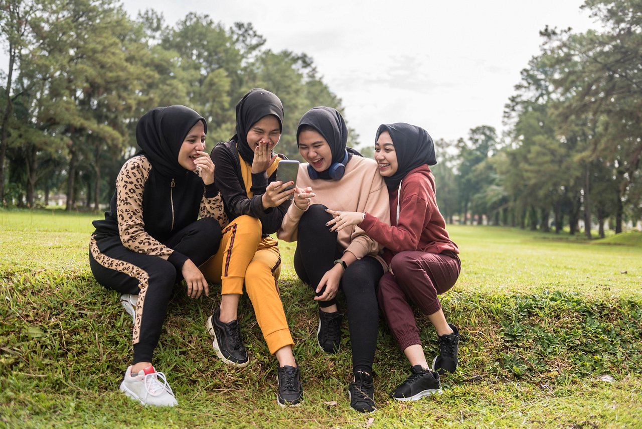 一群頭戴頭巾、身著運動服的年輕女性看著手機上的內容大笑。