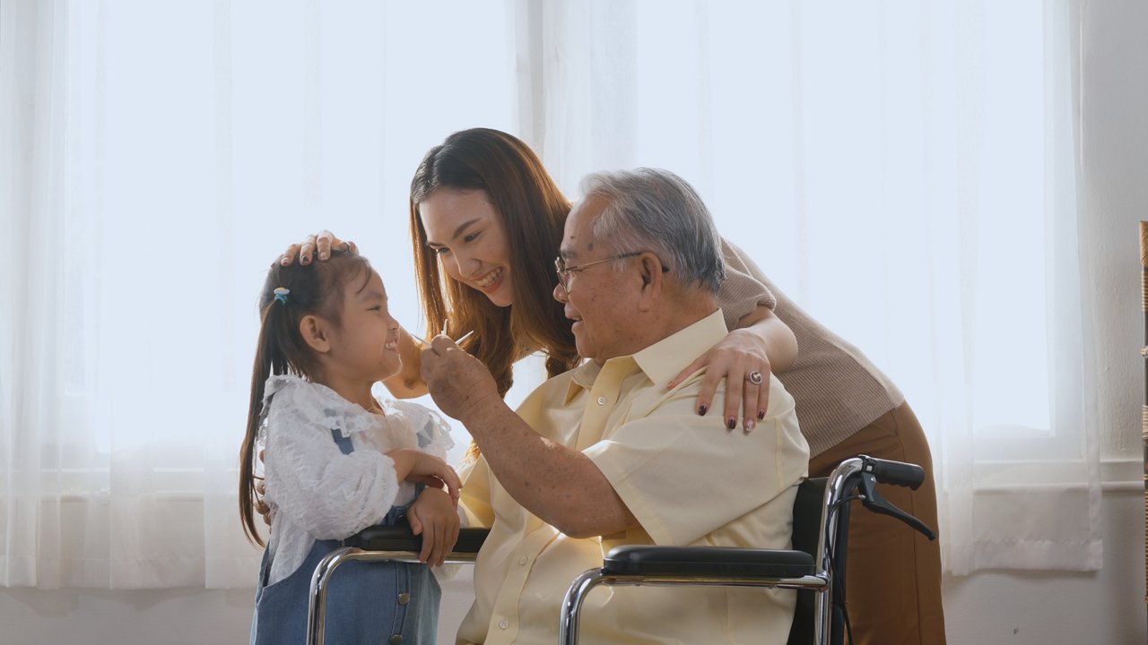 An elderly man in a wheelchair with his daughter and granddaughter in a living room