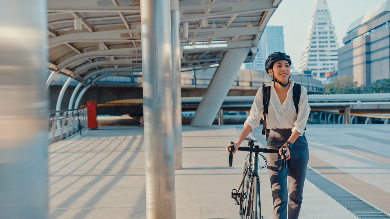 Asian businesswoman go to work at office walk and smile wear backpack look around take bicycle on street around building on a city street. Bike commuting, Commute on bike, Business commuter concept.