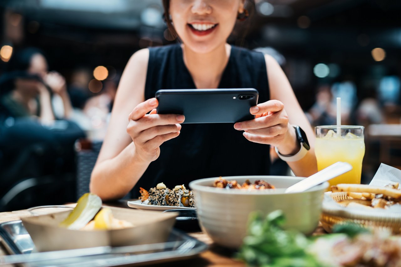 笑容滿面的女子在餐廳裡拍攝食物照片