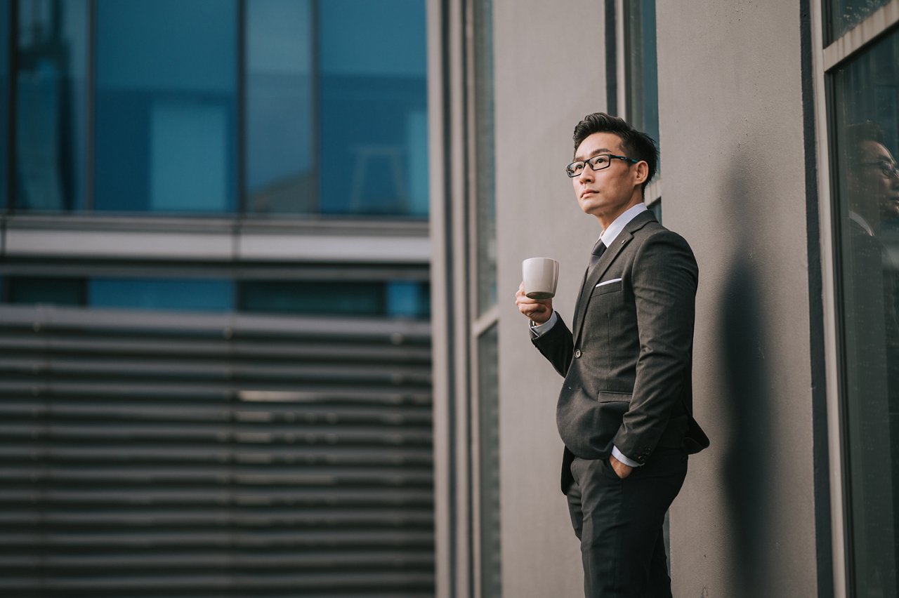 Portrait successful Asian Chinese Businessman holding coffee cup looking away outside office building