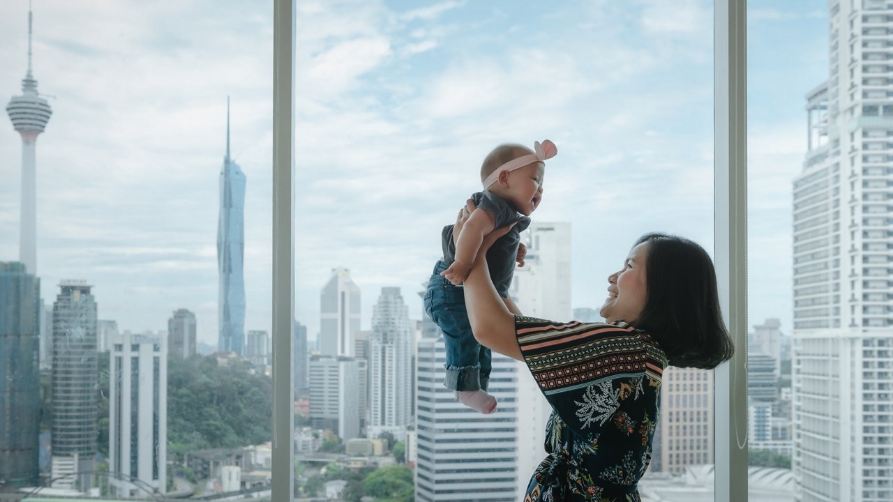 A mom happily lifts her baby up against a backdrop of skyscrapers.