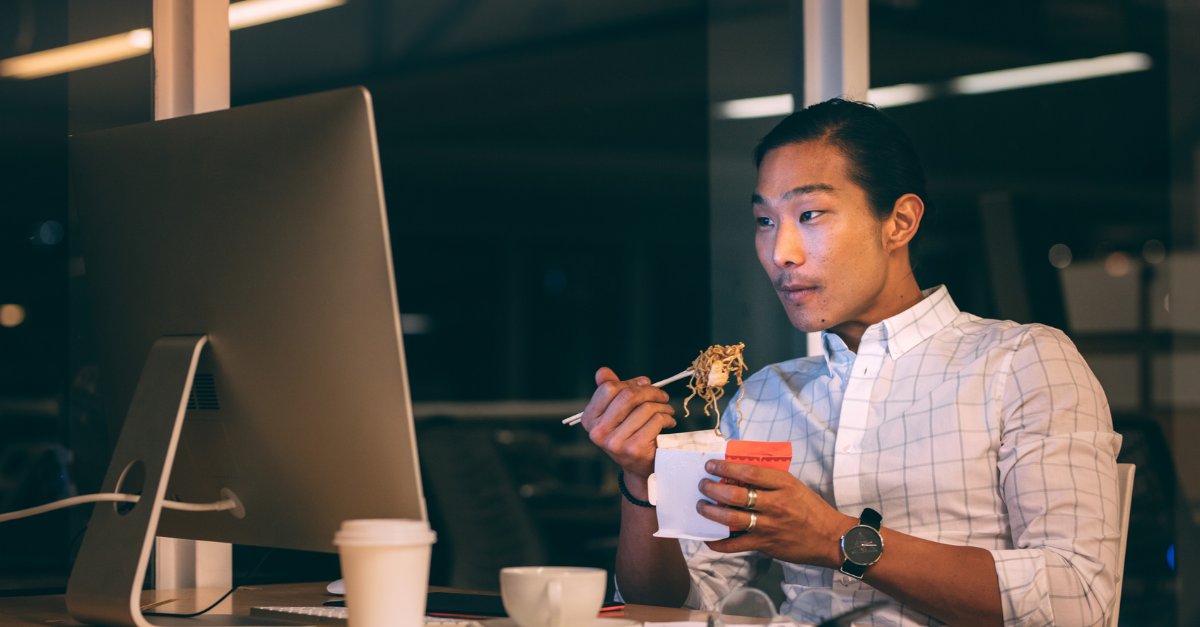 Young man eating instant noodles at her desk while working. 