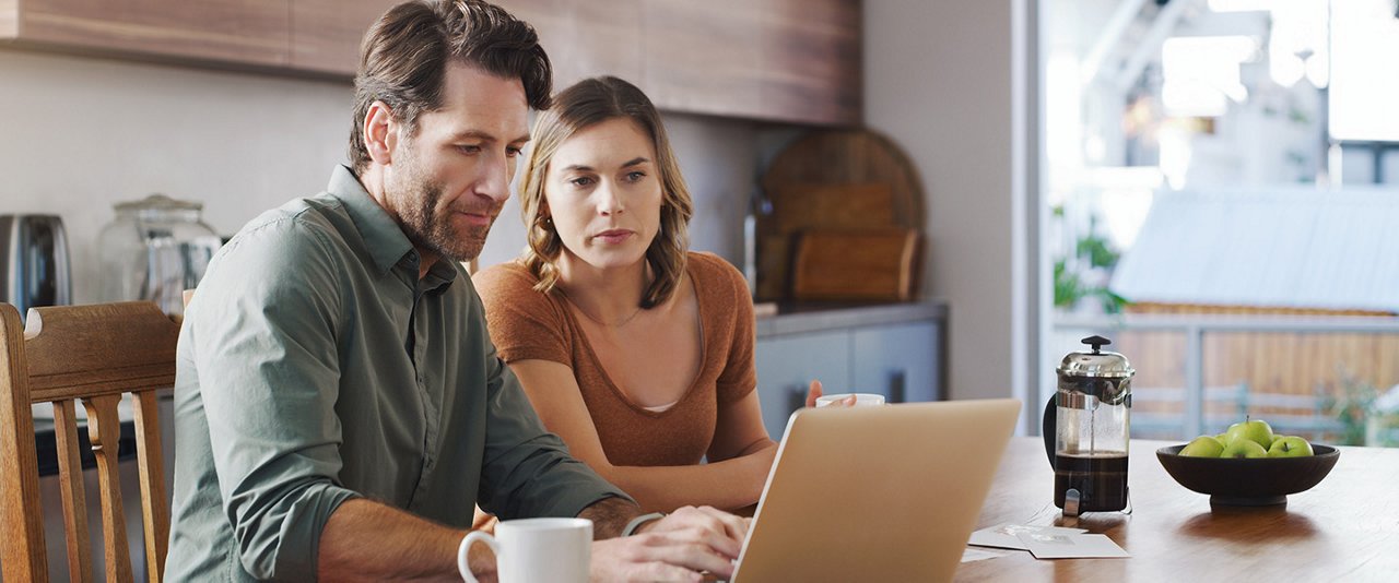 Man and woman in kitchen on their laptop