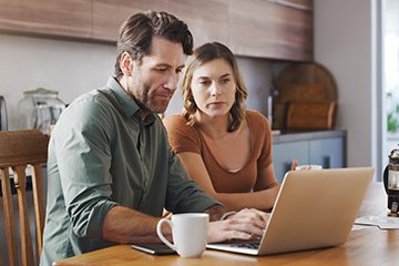 Man and woman in kitchen on their laptop