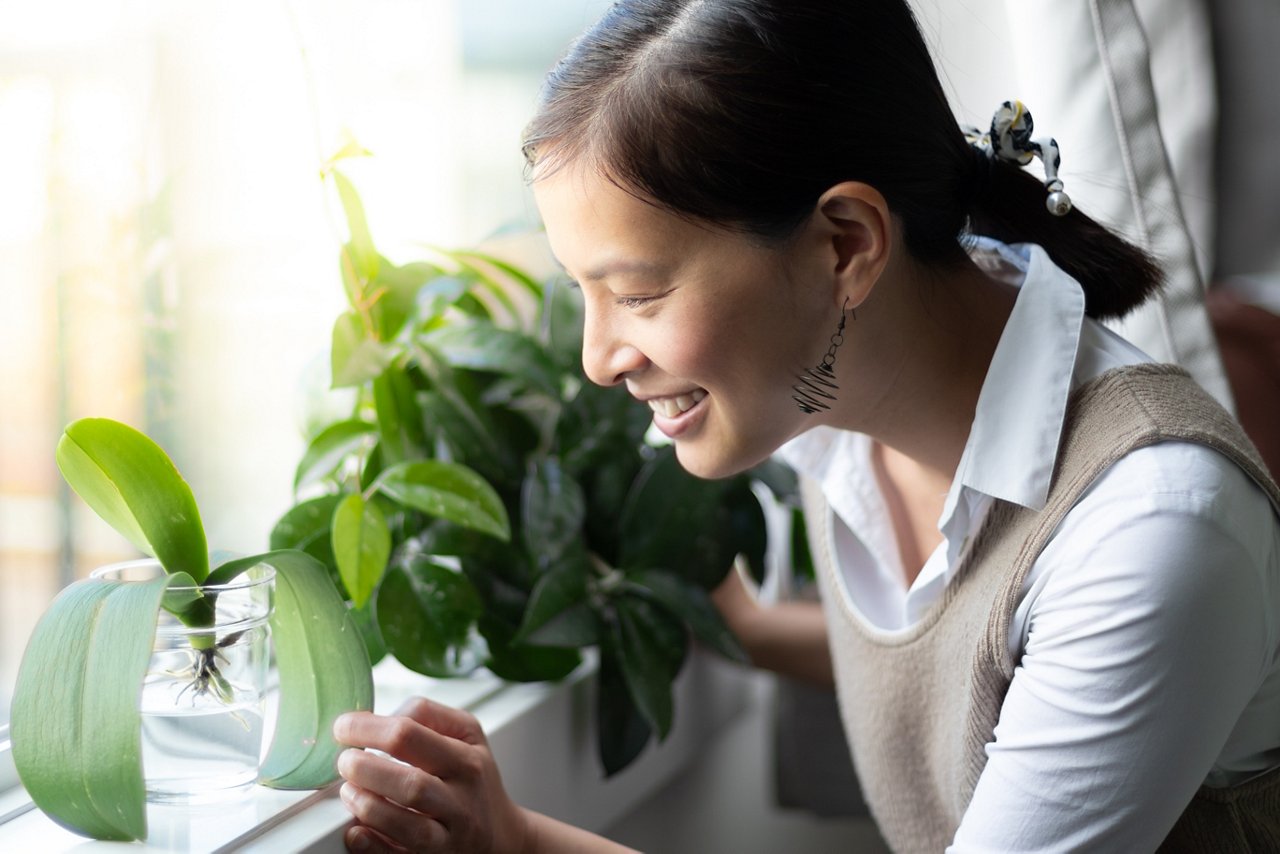 Happy Asian woman checking on her plants by the window