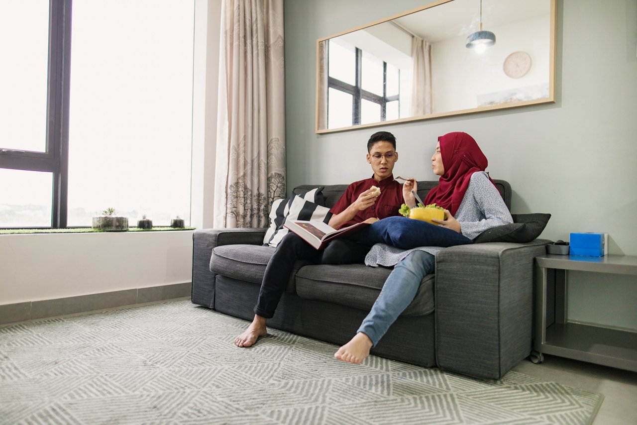 Asian couple having a conversation while eating on a couch