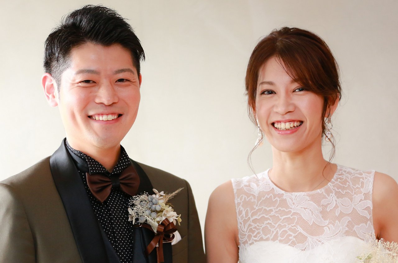 An Asian couple smiles to the camera in their wedding suit and dress