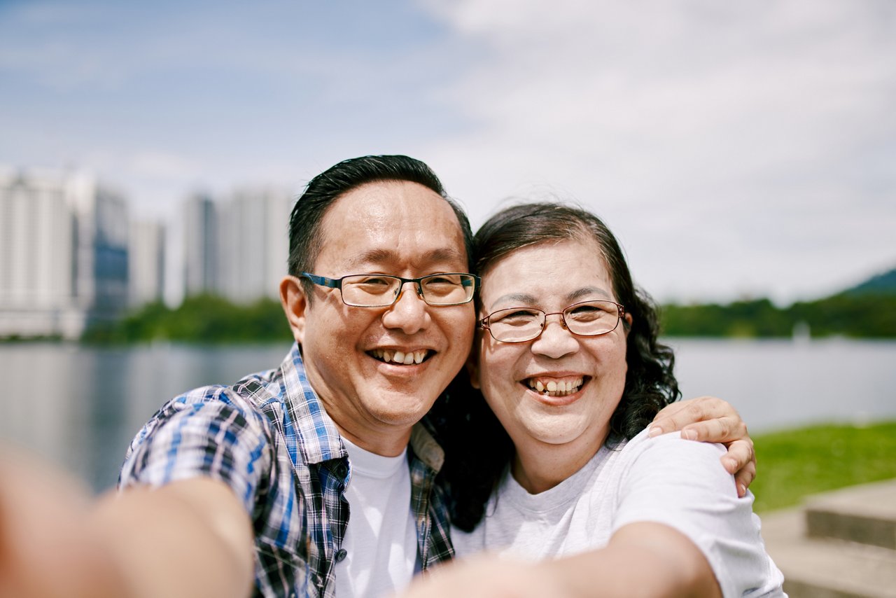 A smiling senior couple wearing glasses is taking a selfie outdoors