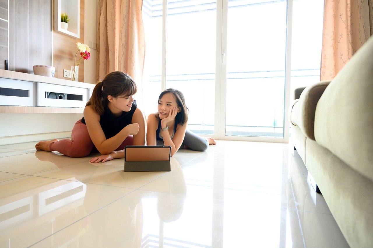 Two Asian women in gym clothes lying on the floor in front of a tablet