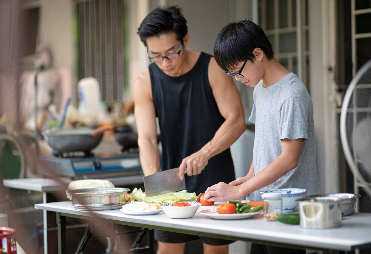Father and son preparing and cutting vegetables in an outdoor kitchen
