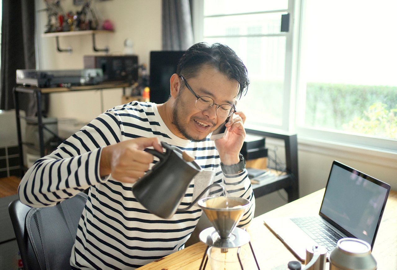 亞裔男子在辦公桌上一邊打電話，一邊沖咖啡