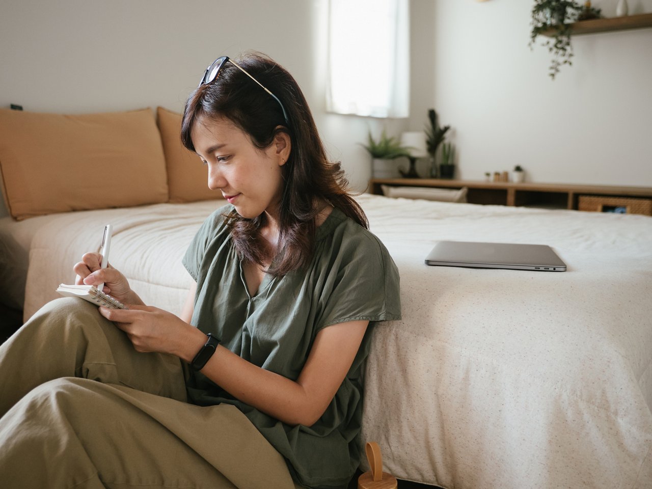 A woman like writing about her work or planning on the notepad at home in the bed room.