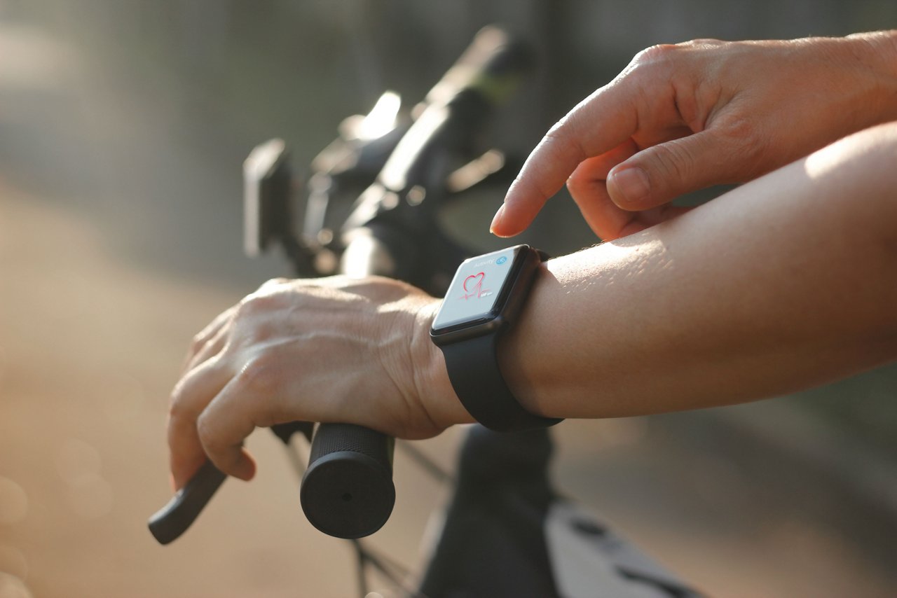 女單車手配戴著帶有心率圖示的智能手錶，在夏季的車道上踏單車