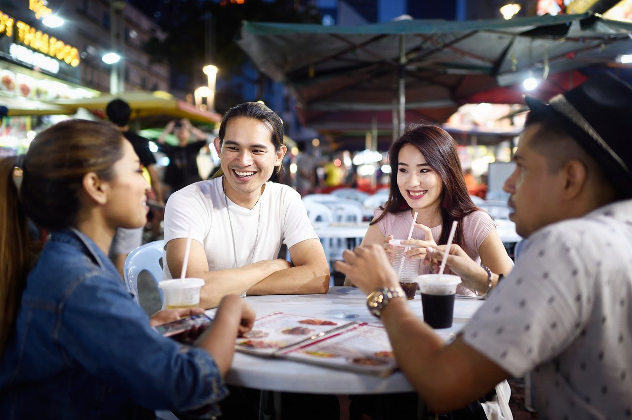 Four friends sitting around an outdoor restaurant table with drinks