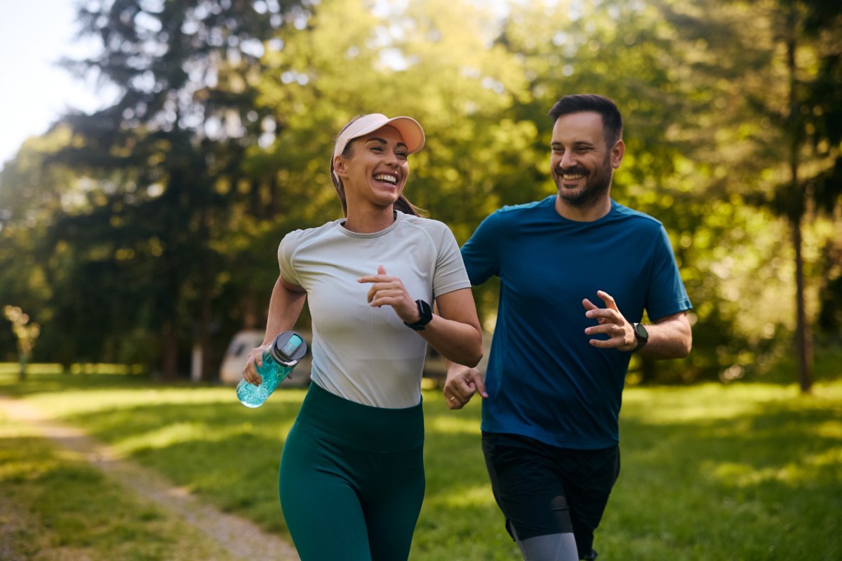 A man and woman jogging together in a park, surrounded by greenery and a clear blue sky.