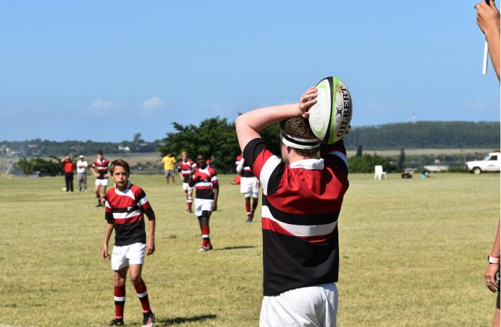 A young boy proudly lifts a rugby ball into the air, symbolizing his love for rugby and playful spirit.