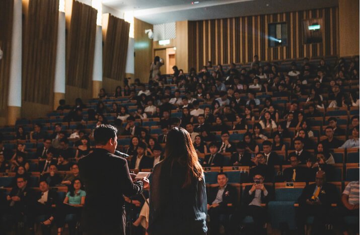 A man and woman address a large audience, showcasing their leadership and connection with the crowd.