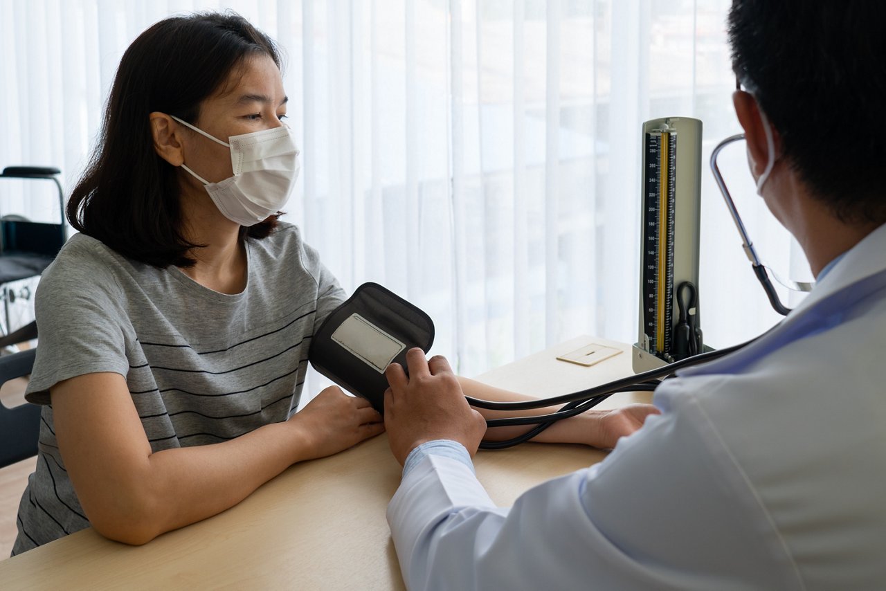 Asian doctor using sphygmomanometer to measure blood pressure of the woman patient that has hypertension and visit him at clinic of hospital. healthcare and medical concept