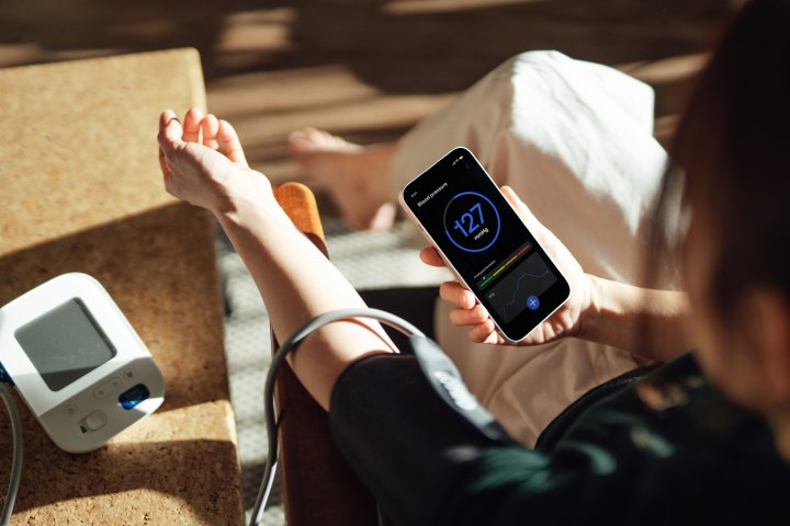 Woman using a blood pressure monitor and smartphone app to track blood pressure readings and manage hypertension risk.