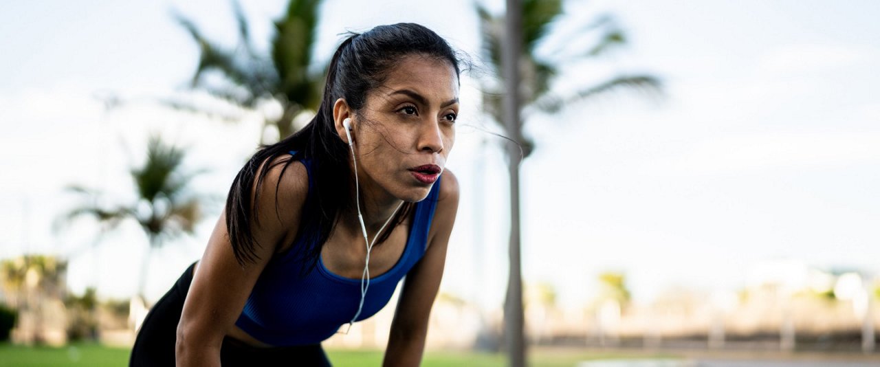 A woman jogs in the park, wearing earphones, enjoying her workout amidst the greenery.