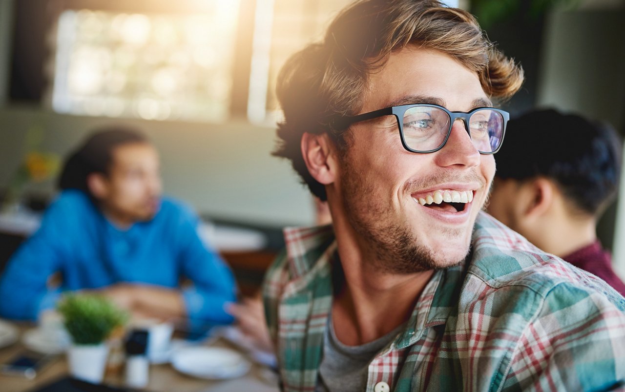 Young man wearing glasses, turning around and smiling into the distance.