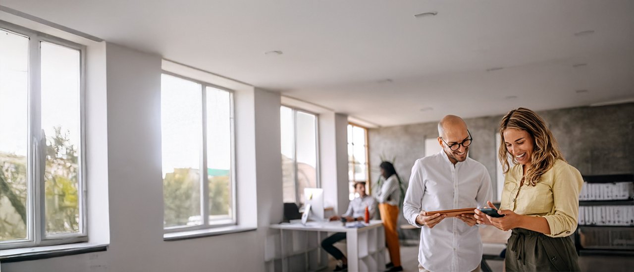 In an office setting, two people are focused on a tablet, collaborating on a task or sharing information.