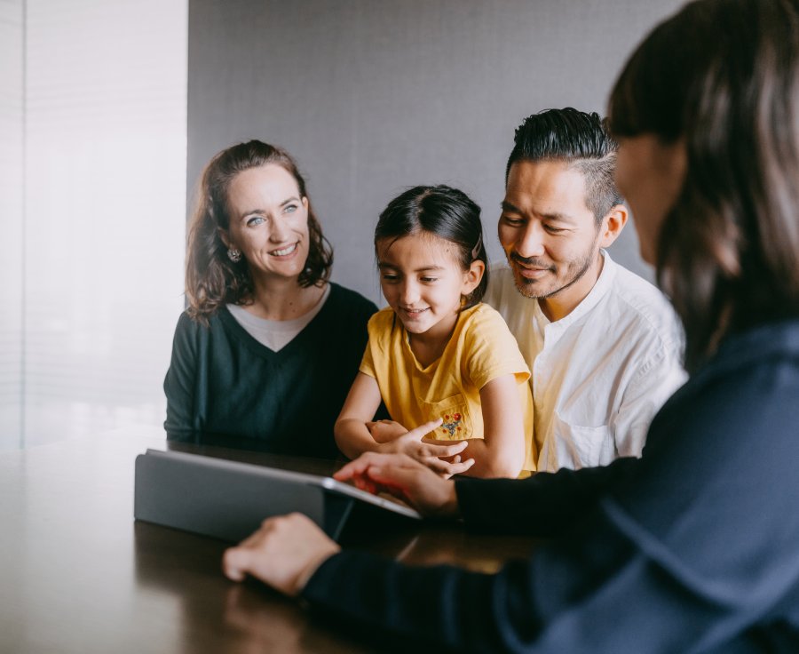 A family gathered around a table, engaging with a tablet computer together, sharing smiles and conversation.