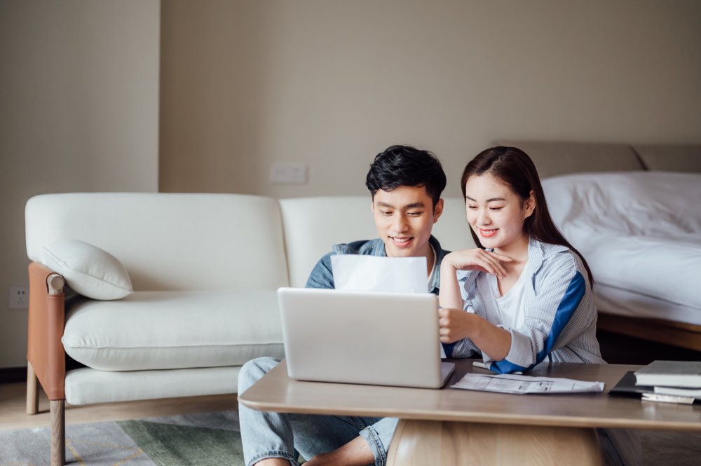 Young couple reviewing information on a laptop and documents at home, exploring whole life critical illness insurance coverage guides and plan comparisons.