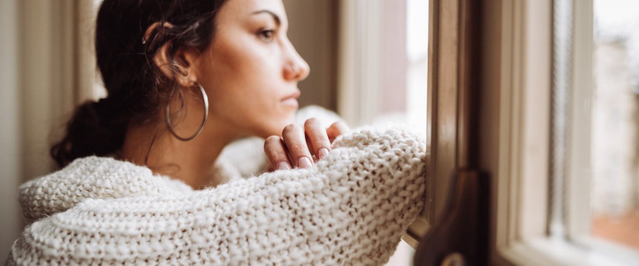 A woman gazes thoughtfully out of a window, lost in her reflections and the view beyond.