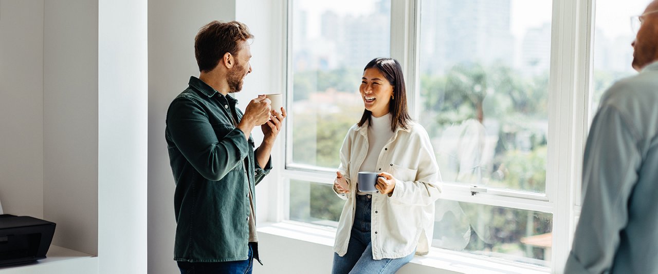 A man and woman sit in an office, enjoying coffee together while engaged in conversation.