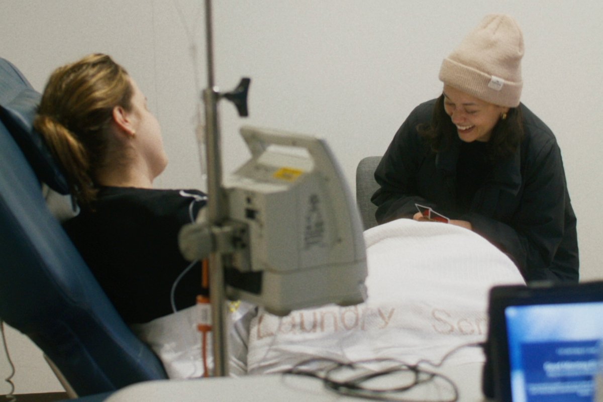 A woman lies in a hospital bed talking to a friend who is visiting.