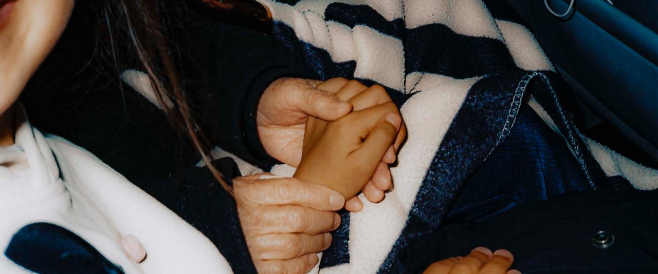 A young child and a woman holding hands in the car.