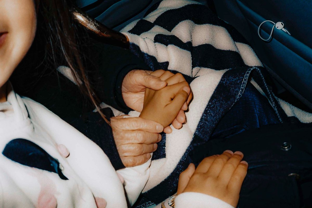 A young child and a woman holding hands in the car.